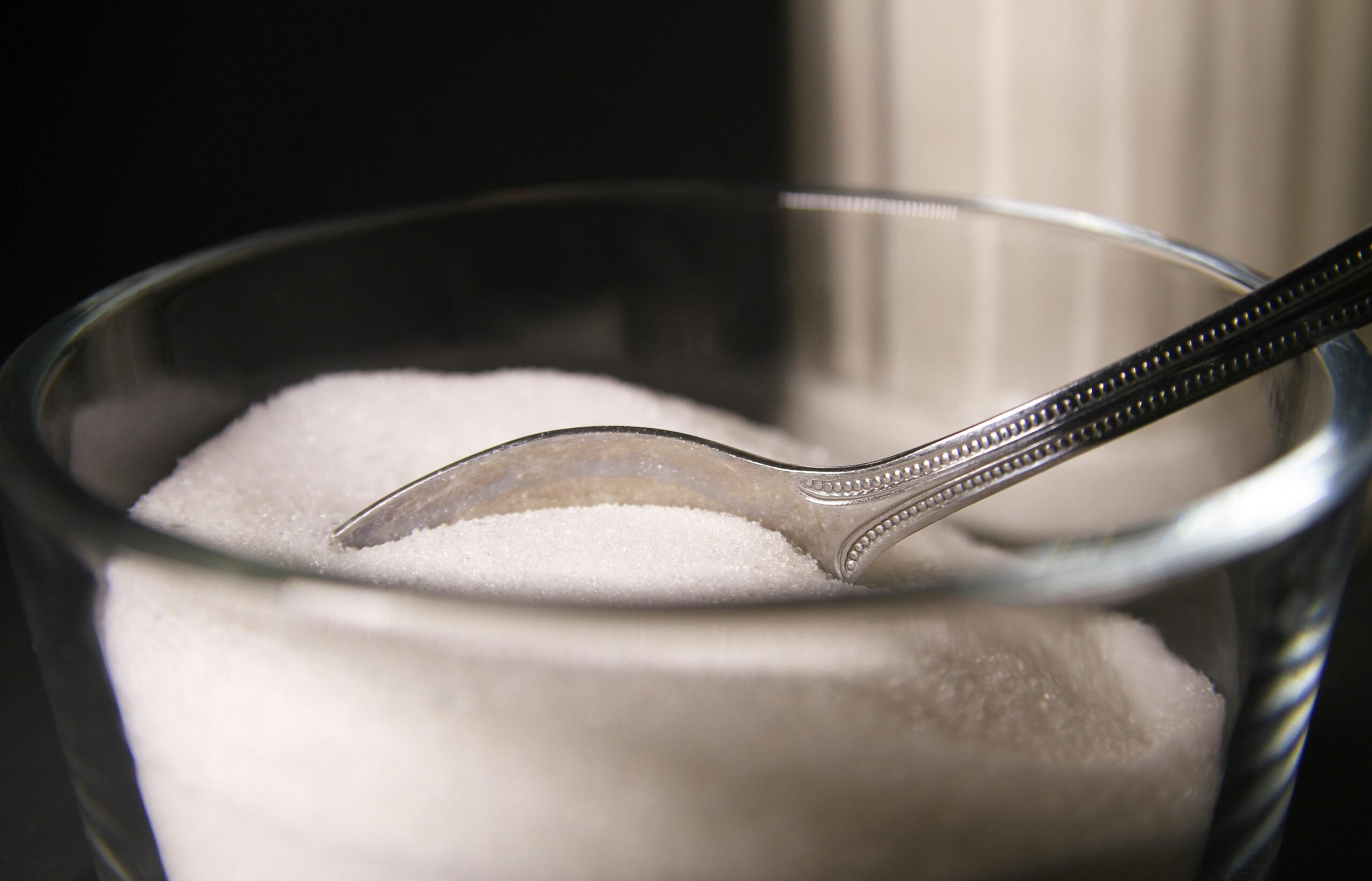 Detailed shot of granulated sugar in a glass bowl featuring a spoon.